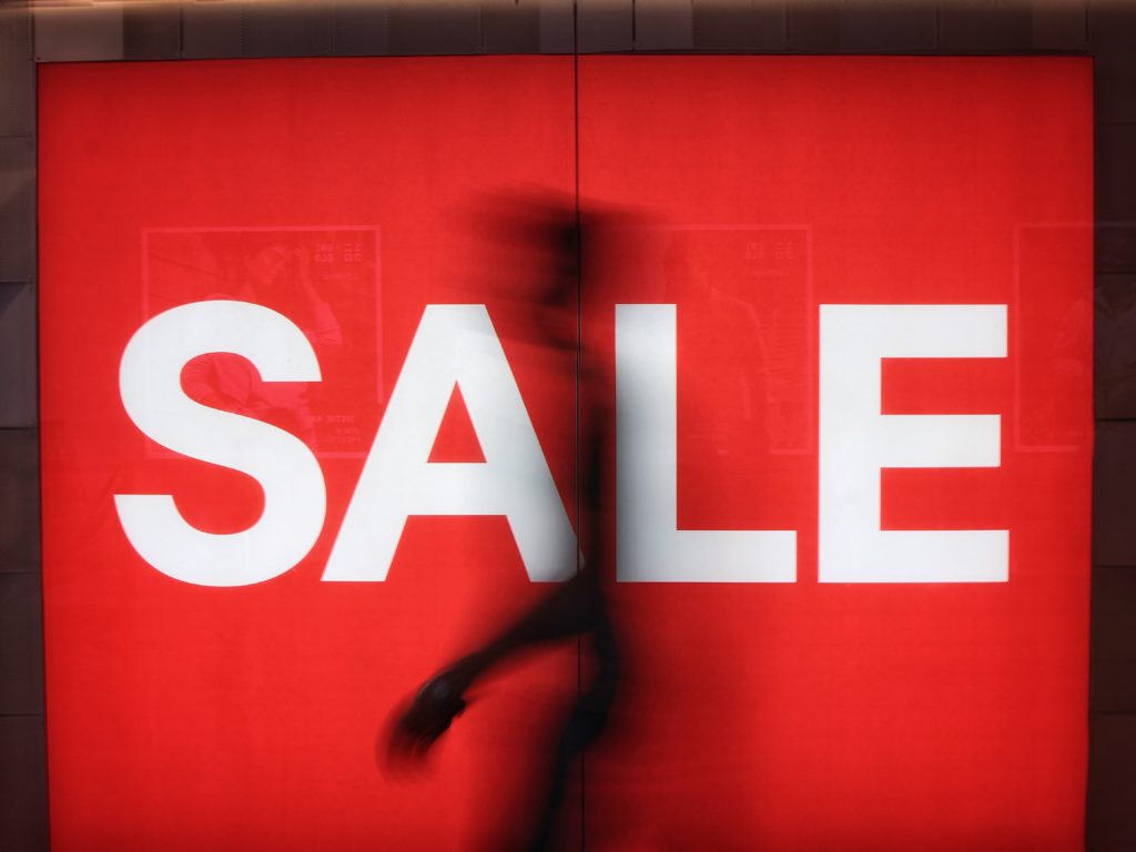 person walking in front of a large sale sign in a store window