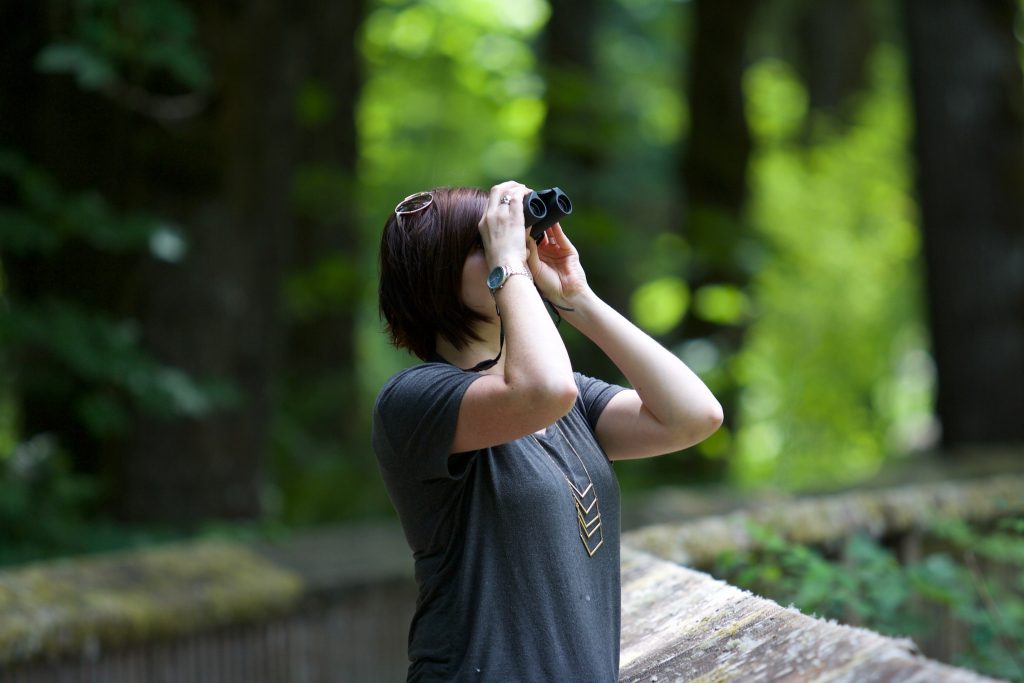 woman searching with binoculars in the woods