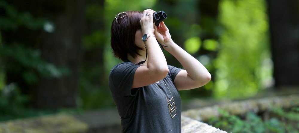 woman searching with binoculars in the woods