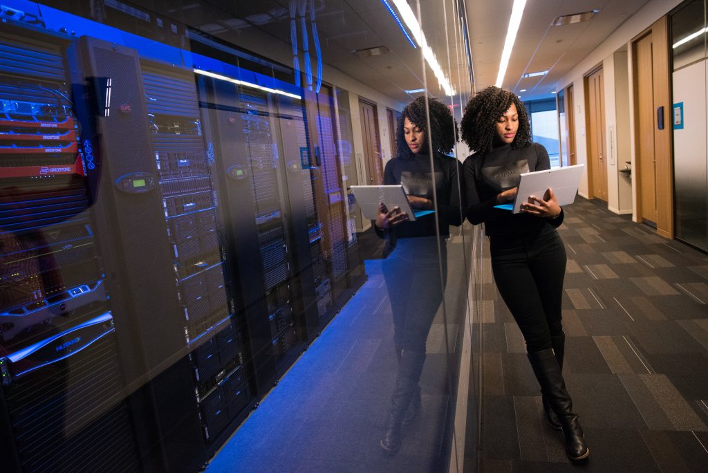 woman standing in a hallway using her laptop next to data