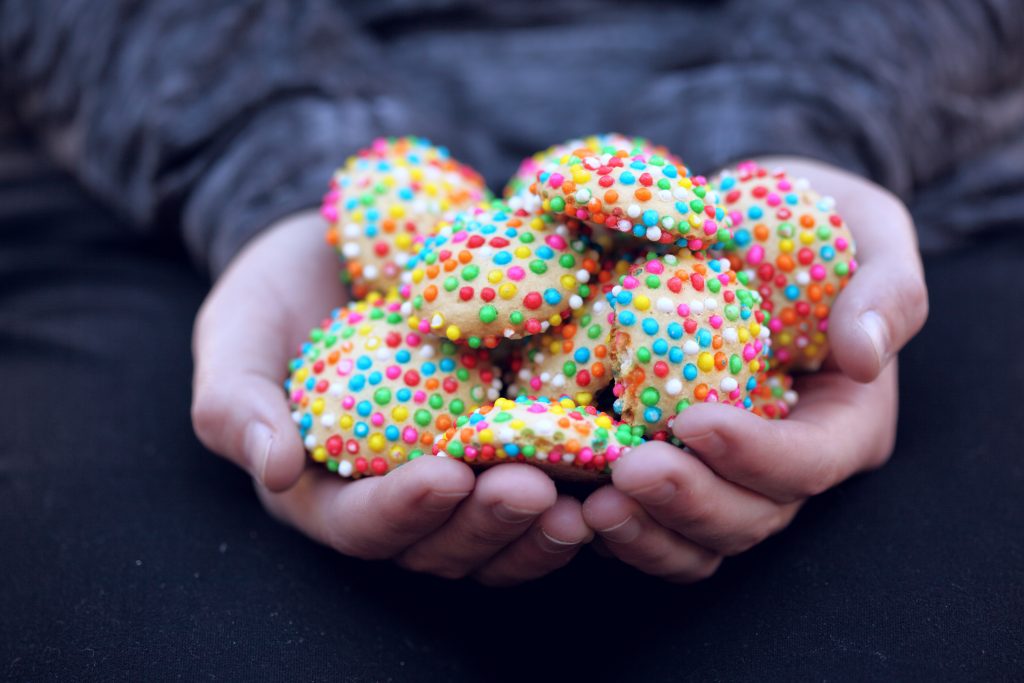 person holding two handfuls of rainbow sprinkle cookies