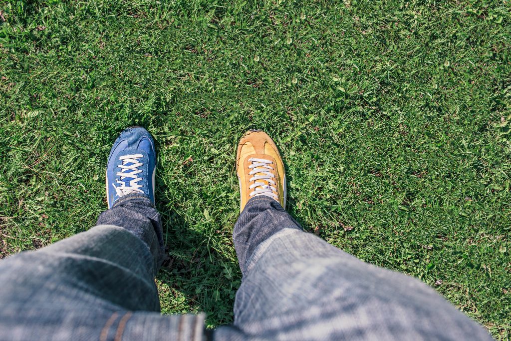 person wearing one blue shoe and one yellow shoe on grass