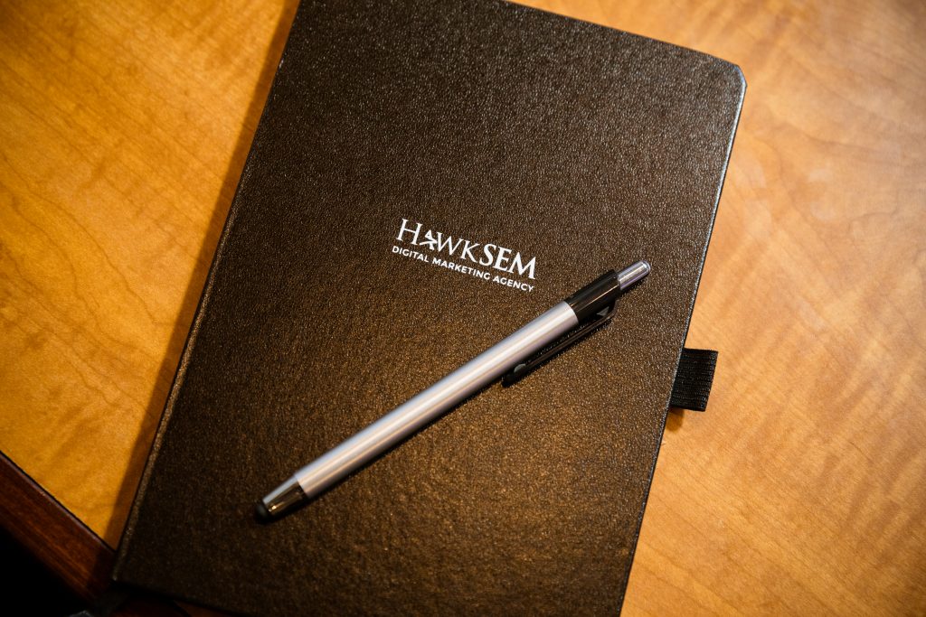 black notebook with hawksem logo and a silver pen on top