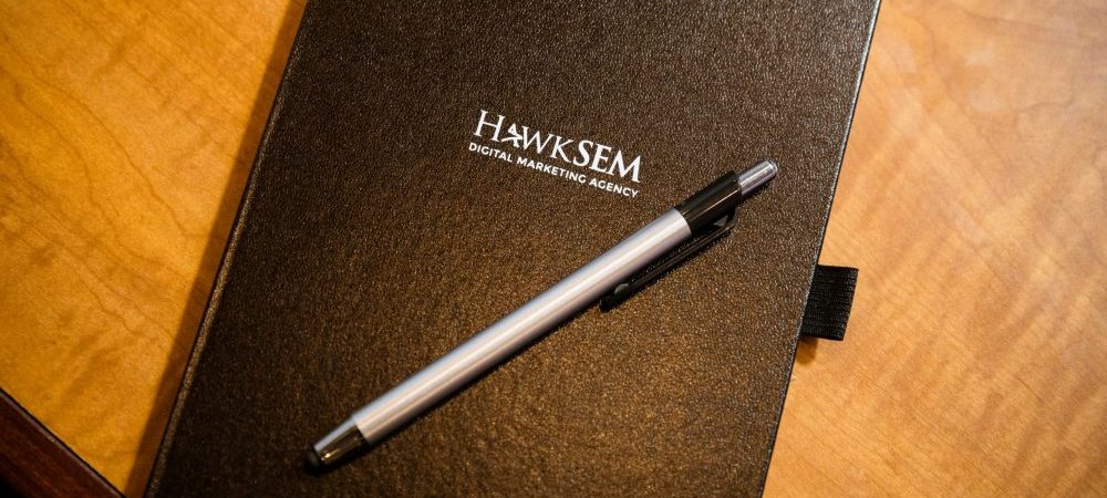 black notebook with hawksem logo and a silver pen on top
