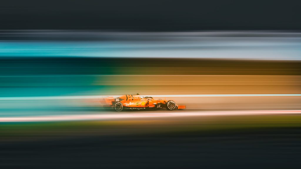 orange car zooming by on a racetrack