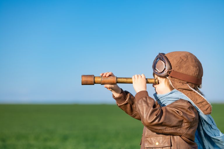 child looking through spyglass outdoor in spring green field. Kid having fun against blue sky background. Discovery concept