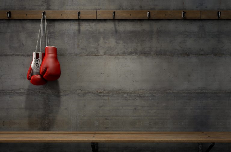 Spotlit boxing gloves hanging on a hanger above an empty wooden bench in a locker change room - 3D render