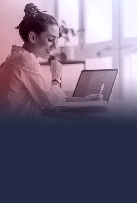 Woman smiling at desk in front of computer with a pen in hand