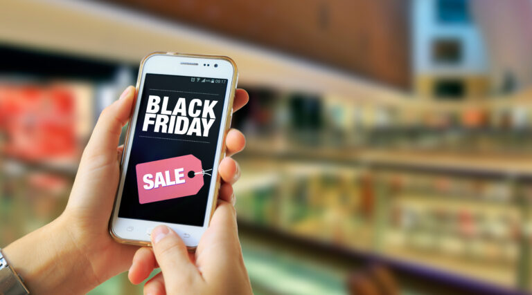 Black Friday. Girl in a Shopping Mall holding a smartphone with a Black Friday advertising on the screen. Marketing, ecommerce, cell phone publicity.